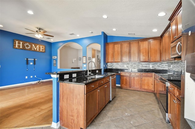 6843 Runner Oak Dr, Wesley Chapel, FL 33545 - kitchen featuring stainless steel appliances, a sink, brown cabinetry, dark stone countertops, and a center island with sink