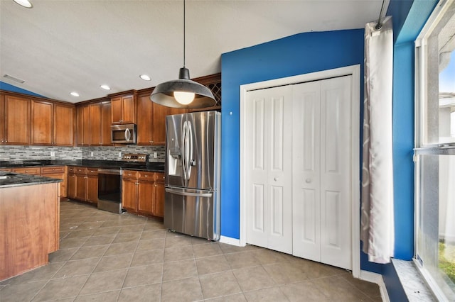 kitchen with appliances with stainless steel finishes, vaulted ceiling, tasteful backsplash, light tile patterned floors, and hanging light fixtures