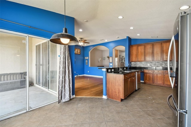 6843 Runner Oak Dr, Wesley Chapel, FL 33545 - kitchen with arched walkways, a kitchen island with sink, hanging light fixtures, freestanding refrigerator, and brown cabinetry