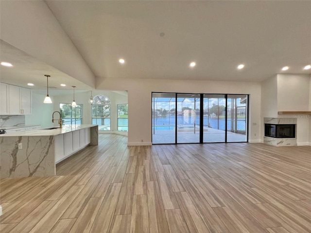 unfurnished living room featuring vaulted ceiling, a fireplace, light hardwood / wood-style flooring, and sink