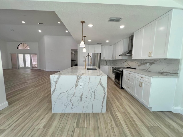 kitchen with tasteful backsplash, a kitchen island with sink, appliances with stainless steel finishes, white cabinets, and wall chimney exhaust hood