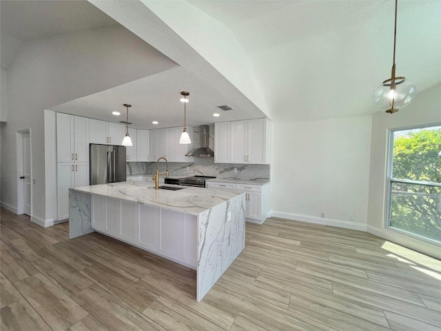 kitchen with vaulted ceiling, a large island with sink, white cabinetry, stainless steel appliances, and wall chimney exhaust hood