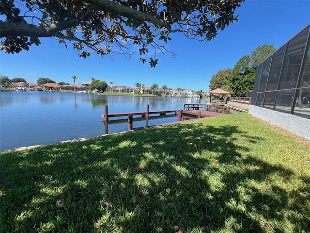 view of dock with a lanai, a water view, and a yard