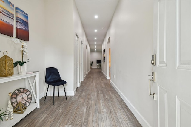 hallway with arched walkways, recessed lighting, wood finished floors, and baseboards