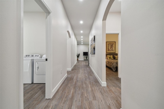 hall with baseboards, arched walkways, wood finished floors, washing machine and clothes dryer, and recessed lighting