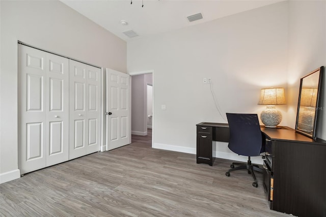 home office featuring a towering ceiling, visible vents, baseboards, and wood finished floors