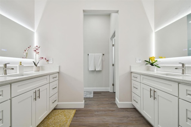 full bathroom with baseboards, two vanities, a sink, and wood finished floors