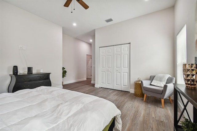 bedroom with wood finished floors, visible vents, a ceiling fan, baseboards, and a closet