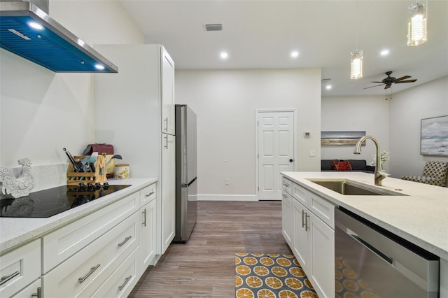 kitchen with wall chimney exhaust hood, appliances with stainless steel finishes, decorative light fixtures, white cabinetry, and a sink