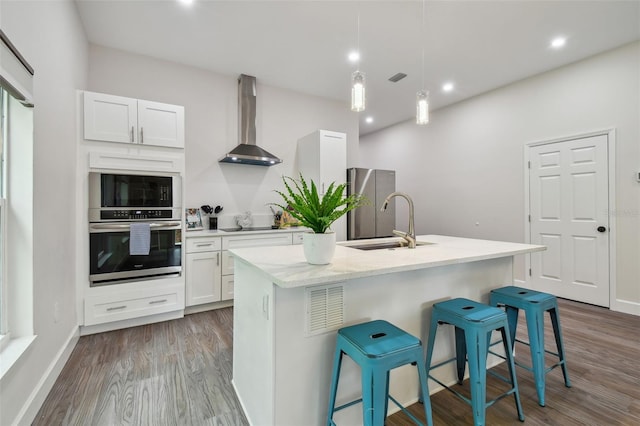 kitchen with wall chimney exhaust hood, stainless steel oven, a sink, and wood finished floors