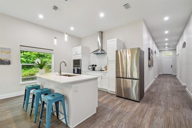 kitchen featuring a sink, visible vents, wall chimney range hood, appliances with stainless steel finishes, and a center island with sink