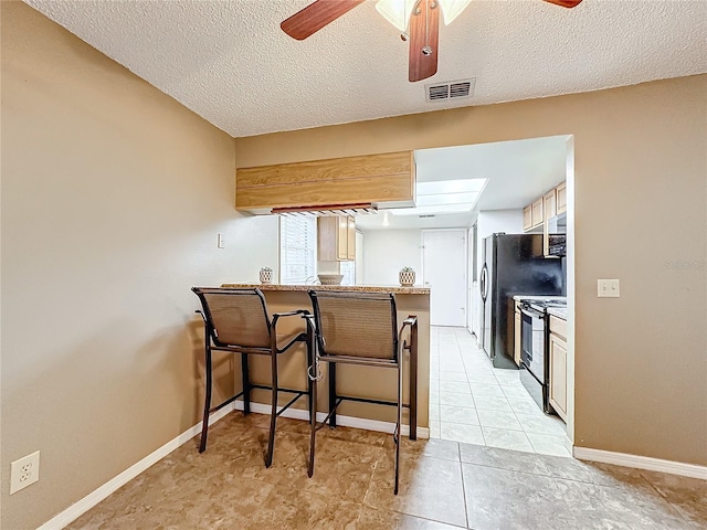 kitchen with a peninsula, electric range, visible vents, light countertops, and a kitchen bar