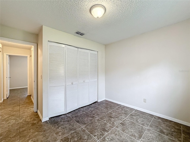 unfurnished bedroom featuring baseboards, a textured ceiling, visible vents, and a closet