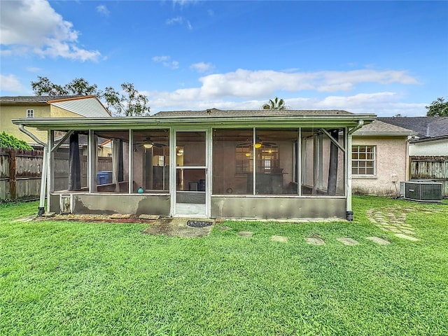 rear view of property with central air condition unit, a sunroom, fence, and a lawn