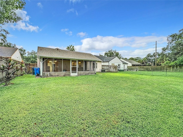 rear view of house featuring a lawn, a fenced backyard, and a sunroom