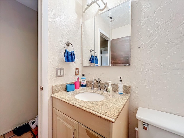 half bath with a textured wall, vanity, and toilet