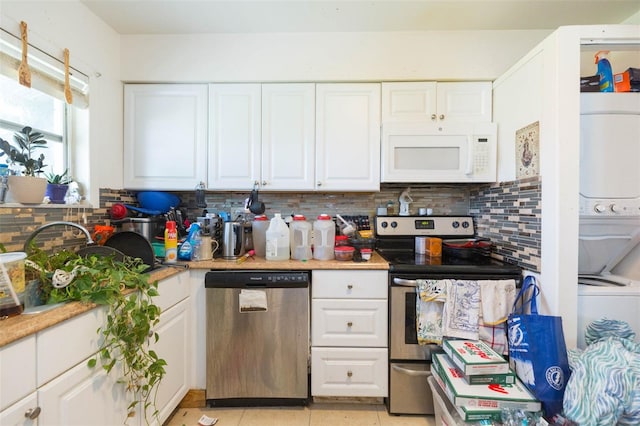 kitchen with backsplash, stainless steel appliances, white cabinetry, stacked washer / dryer, and light tile patterned flooring