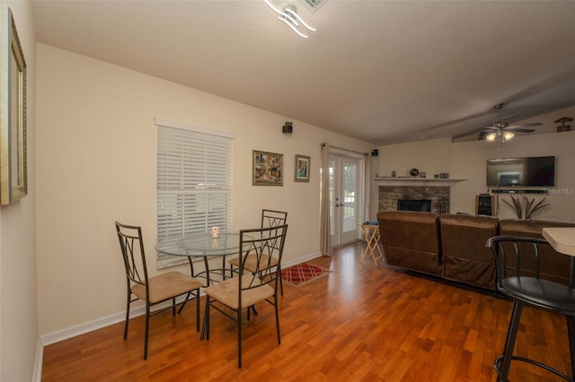 dining room with ceiling fan, vaulted ceiling, a stone fireplace, and hardwood / wood-style flooring