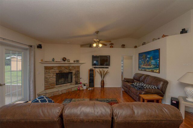 living room with ceiling fan, vaulted ceiling, hardwood / wood-style floors, and a stone fireplace