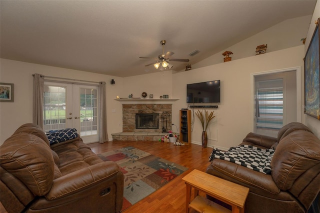 living room with ceiling fan, a stone fireplace, hardwood / wood-style floors, vaulted ceiling, and french doors