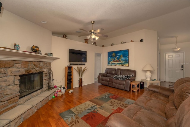 living room featuring ceiling fan, a textured ceiling, vaulted ceiling, a stone fireplace, and hardwood / wood-style flooring