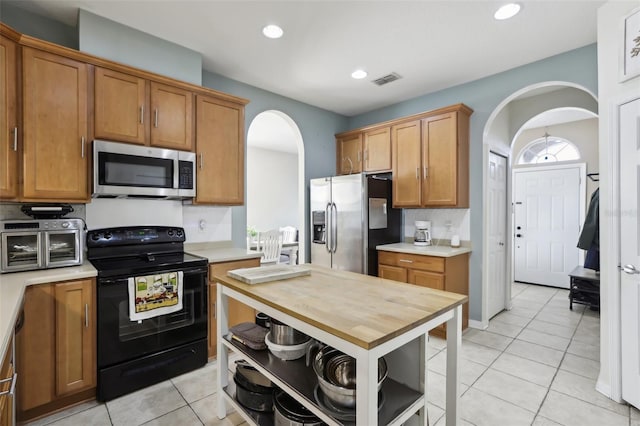 7720 Rathdown Ln, Wesley Chapel, FL 33545 - kitchen featuring appliances with stainless steel finishes, arched walkways, light tile patterned floors, open shelves, and brown cabinets