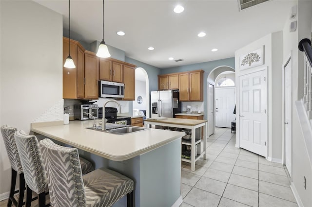7720 Rathdown Ln, Wesley Chapel, FL 33545 - kitchen featuring appliances with stainless steel finishes, arched walkways, a peninsula, light countertops, and brown cabinetry