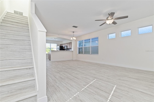 unfurnished living room with ceiling fan with notable chandelier and light wood-type flooring