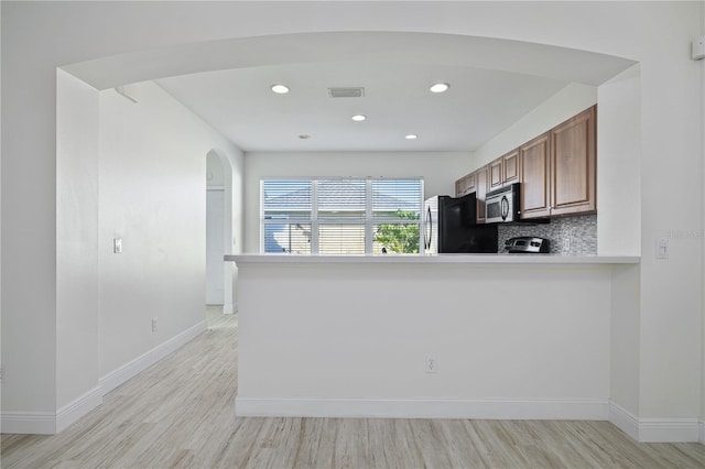 kitchen with appliances with stainless steel finishes, light wood-type flooring, kitchen peninsula, and tasteful backsplash