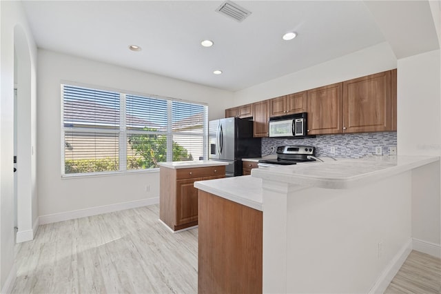 kitchen with appliances with stainless steel finishes, kitchen peninsula, light hardwood / wood-style flooring, and tasteful backsplash