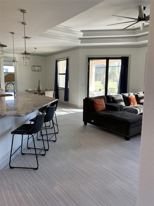 living room featuring a raised ceiling, ceiling fan, crown molding, and sink