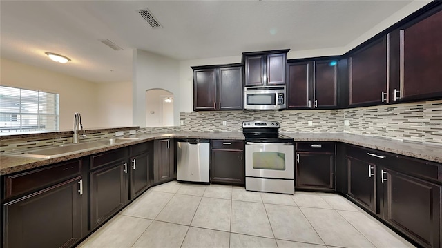 kitchen with backsplash, light tile patterned floors, appliances with stainless steel finishes, stone countertops, and sink