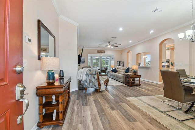 living room featuring hardwood / wood-style flooring, ceiling fan with notable chandelier, and crown molding