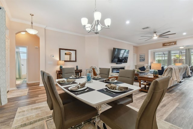 dining space with hardwood / wood-style floors, ceiling fan with notable chandelier, and ornamental molding