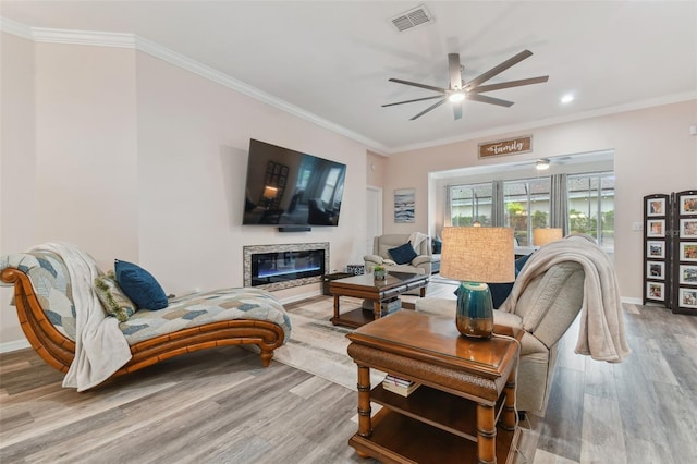 living room featuring visible vents, wood finished floors, a glass covered fireplace, and crown molding