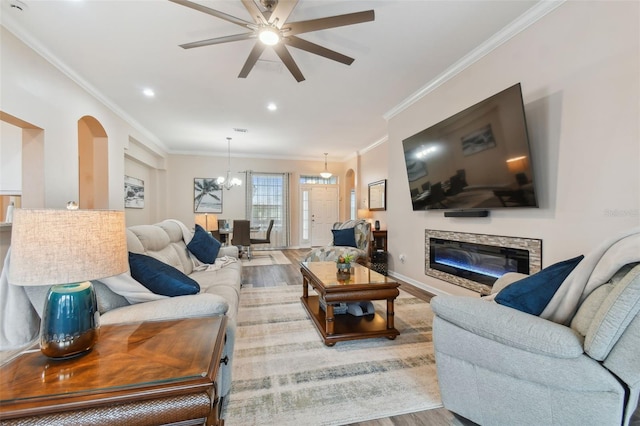 living room with a fireplace, light hardwood / wood-style flooring, ceiling fan with notable chandelier, and ornamental molding