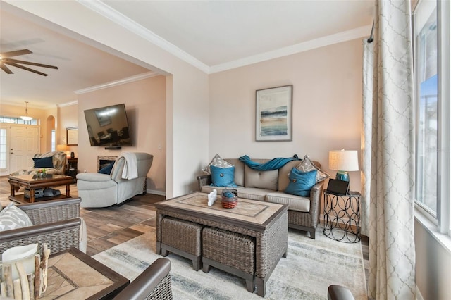 living area featuring ceiling fan, arched walkways, wood finished floors, and crown molding