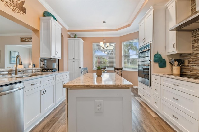 kitchen with ornamental molding, a sink, backsplash, appliances with stainless steel finishes, and wall chimney range hood