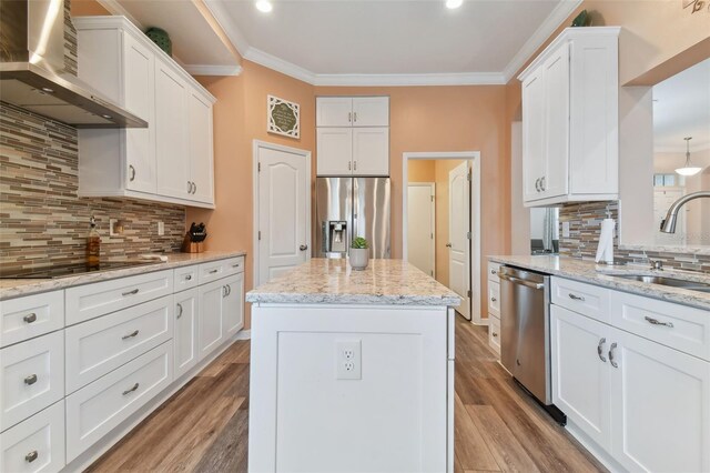 kitchen featuring backsplash, sink, appliances with stainless steel finishes, wall chimney exhaust hood, and a kitchen island