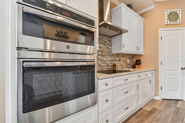 kitchen featuring light hardwood / wood-style flooring, wall chimney exhaust hood, decorative backsplash, white cabinetry, and crown molding