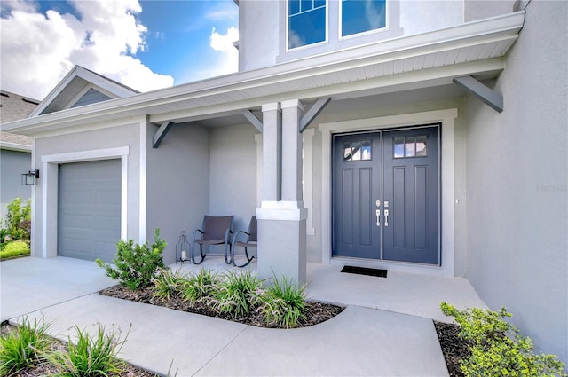 entrance to property with covered porch, an attached garage, and stucco siding