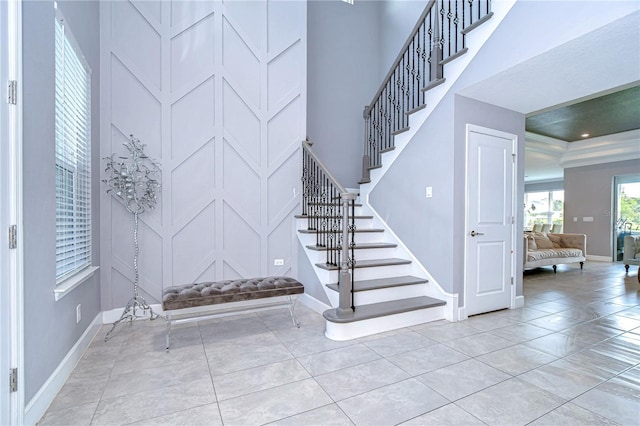 entryway featuring stairs, light tile patterned floors, a towering ceiling, and baseboards