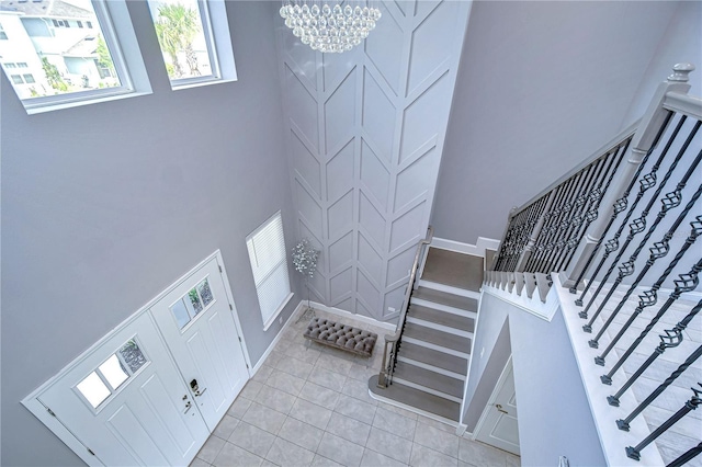 foyer entrance with baseboards, a towering ceiling, stairway, a chandelier, and light tile patterned flooring