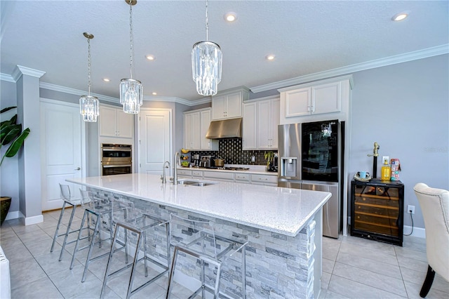 kitchen featuring tasteful backsplash, wine cooler, stainless steel appliances, under cabinet range hood, and a sink