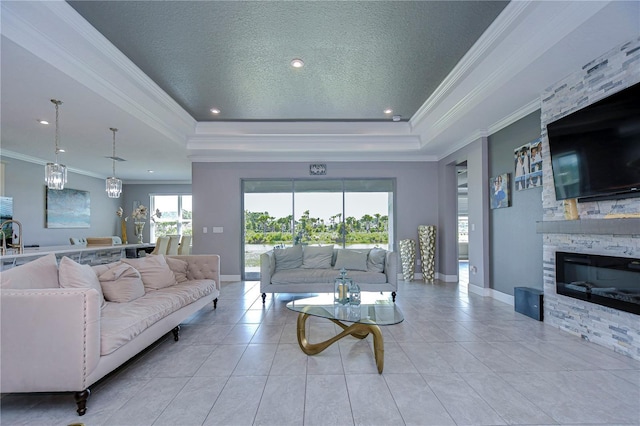 living area with a textured ceiling, a stone fireplace, baseboards, a raised ceiling, and crown molding