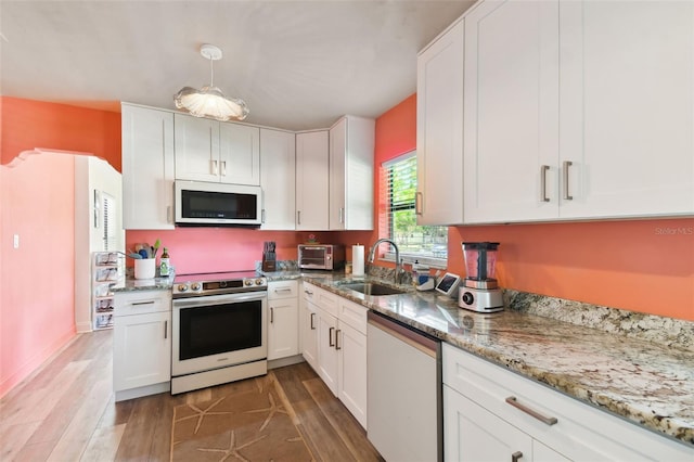 kitchen featuring white cabinets, appliances with stainless steel finishes, light stone counters, sink, and wood-type flooring