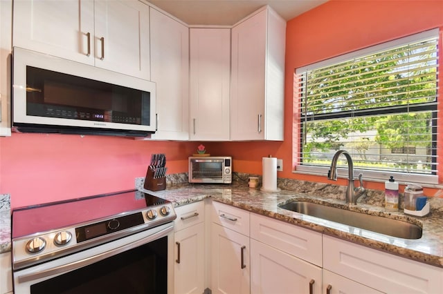 kitchen with white cabinets, light stone countertops, stainless steel appliances, and sink