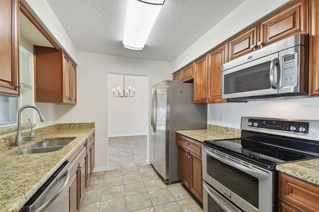 kitchen with light stone counters, a textured ceiling, sink, a notable chandelier, and appliances with stainless steel finishes