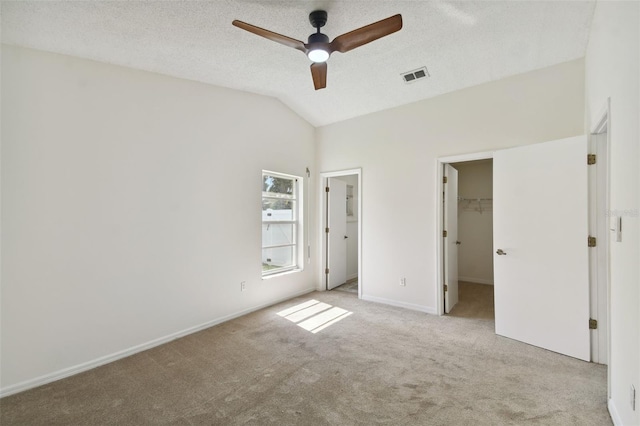 unfurnished bedroom featuring ceiling fan, lofted ceiling, a walk in closet, a closet, and light carpet