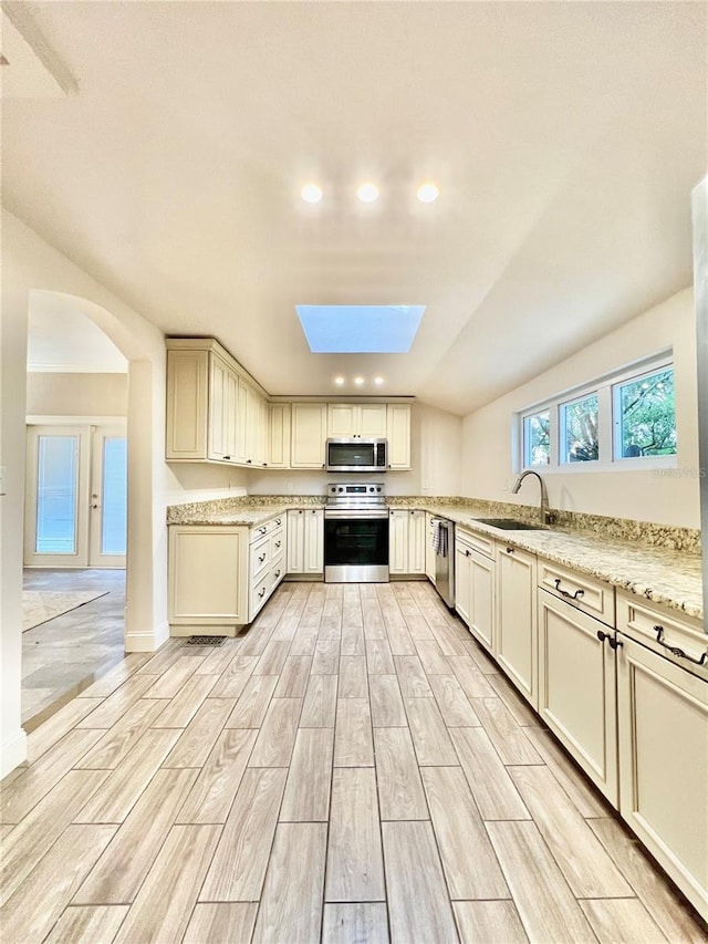 kitchen with light hardwood / wood-style floors, sink, cream cabinets, light stone counters, and appliances with stainless steel finishes